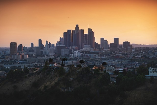 The downtown Los Angeles skyline rises over sandy hills covered in palm trees and houses.