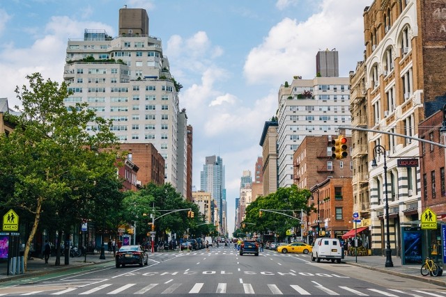 The tree-covered streets of New York are lined with tall buildings, people, and cars.