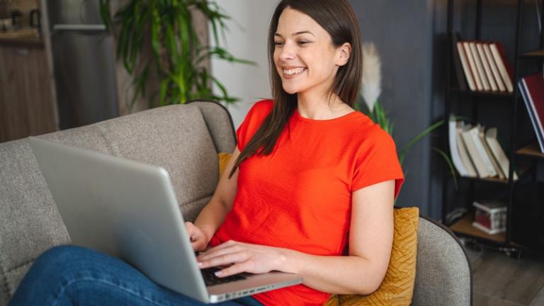 Woman at home on couch browsing on laptop with a smile