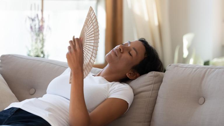 Woman fanning herself in hot apartment without A/C
