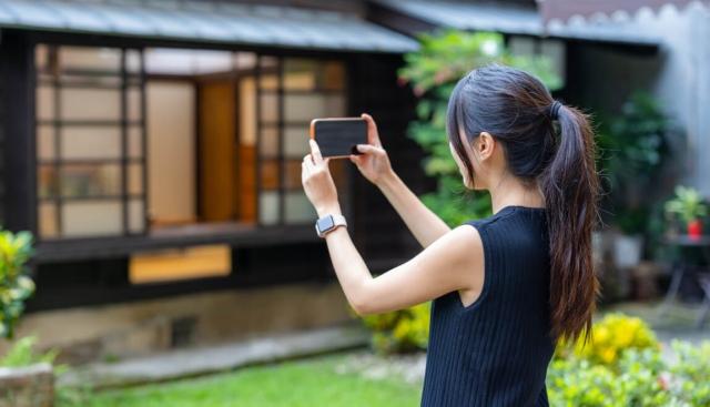 A woman takes pictures of a house with her smartphone.