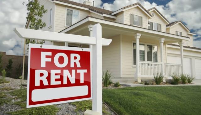 A two-story home in the suburbs with a For Rent sign displayed in the front yard