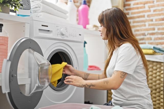 A woman takes her laundry from a clothes dryer and places it in a laundry basket.