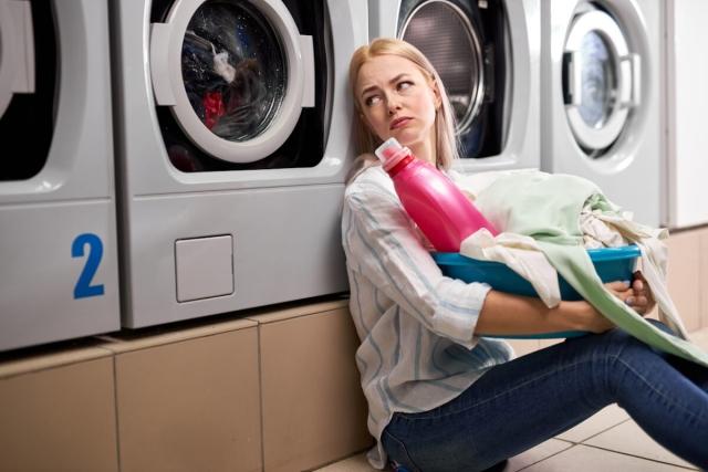 A bored woman watches her laundry in a washer at a laundromat.