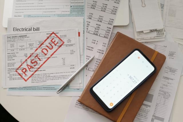 A pile of utility bills marked with a bright red "PAST DUE" stamp sits next to a phone with a calculator app open.