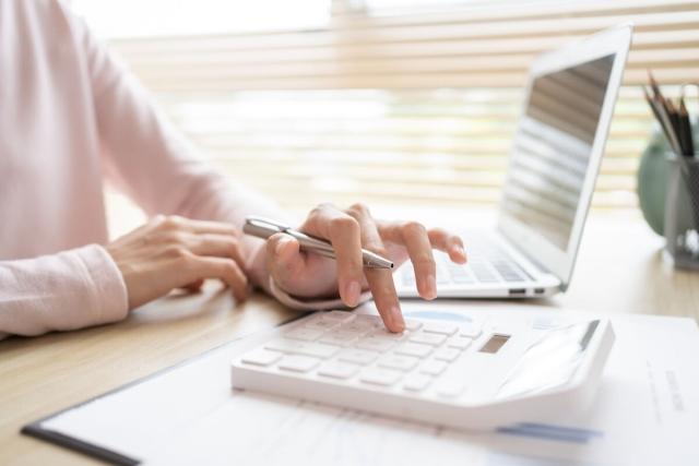A close-up view of a landlord making calculations while looking at something on a laptop.