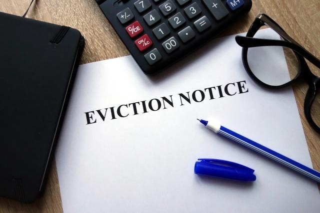Paper with "eviction notice" on the front with a pen on top and a calculator and pair of glasses near.