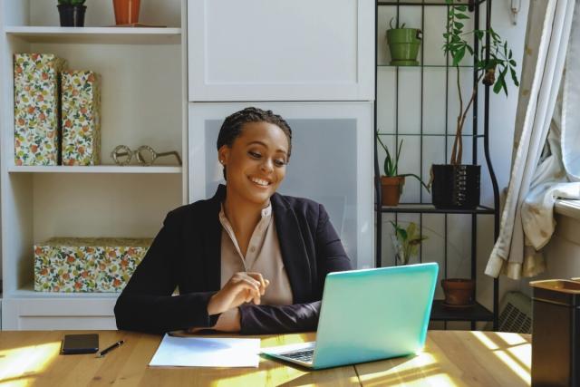 Woman sitting in front of laptop and smiling with hand raised to type.
