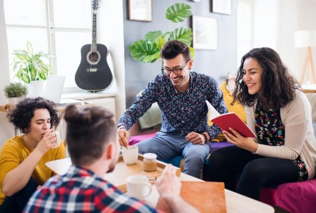 Group of students chatting and drinking coffee on the couch in their apartment.