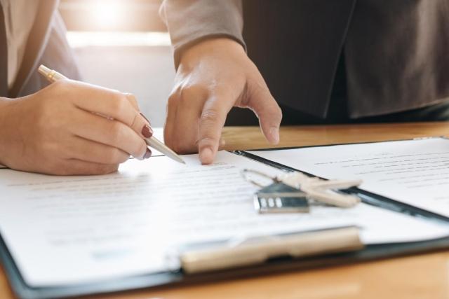 Close-up image of two people reviewing and signing a rental lease agreement with a key fob on the table, symbolizing apartment move-in.