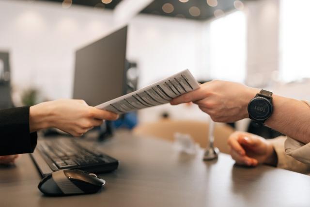 Tenant handing over a printed proof of renters insurance to leasing office staff member inside a modern apartment community office setting.
