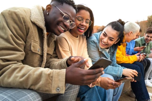 Group of Gen Zers laugh at a phone. 