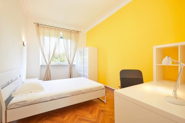 Room for rent with basic furniture and bright yellow wall.
