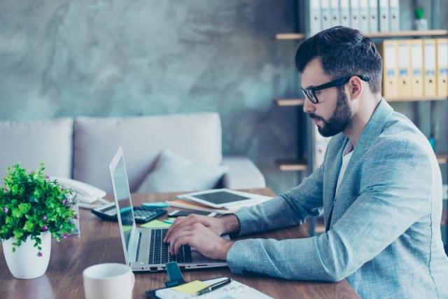 Man in business suit sitting at desk typing on a laptop
