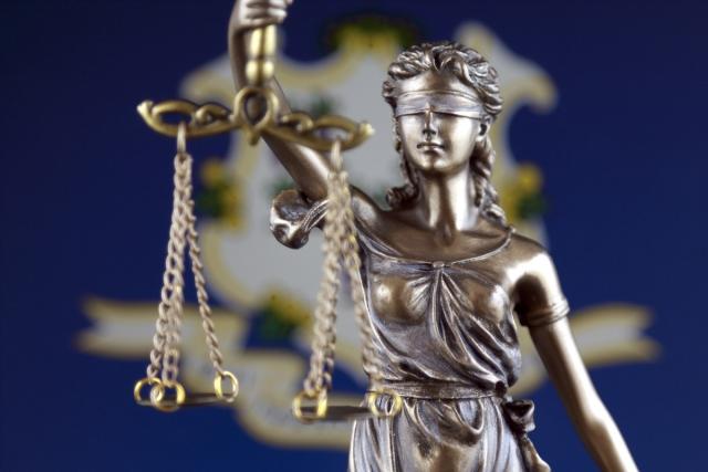A bronze statue of Themis, Greek goddess of law and justice, in front of the Connecticut flag.