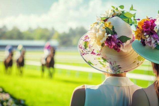 Women in flowery hats watch a horse race.