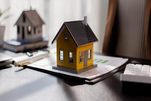 A small toy house sitting on a stack of business papers.