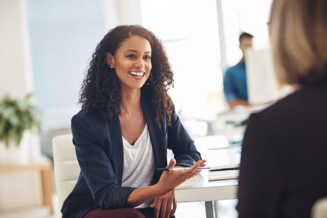 A professionally dressed woman having a table discussion with someone