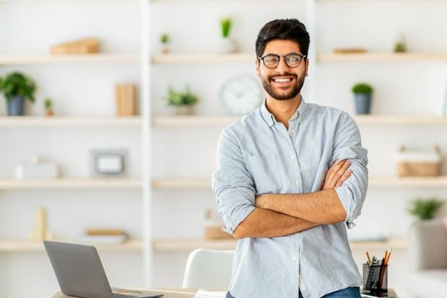 Man standing proudly with his arms folded while leaning against a desk
