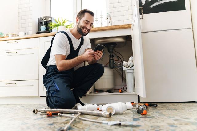 Man in overalls managing maintenance requests on his phone next to sink he is fixing.