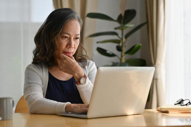 Woman sitting at a table deep in thought while using her laptop 