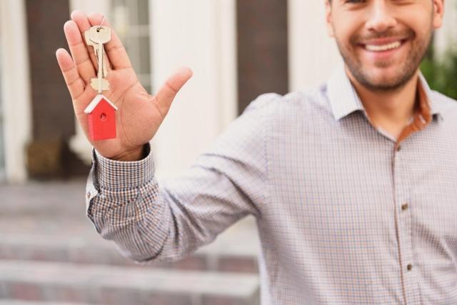 Smiling man holding house keys to his new rental property