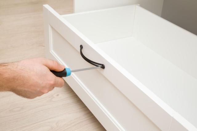 A hand tightening screws on a drawer handle