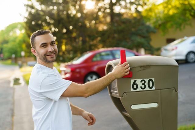 A man checking the red arm on a residential mailbox.