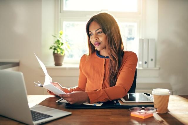A business person sitting at a desk reading documents in her hands.
