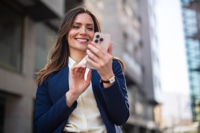 A landlord in a blue suit smiles at her smartphone.
