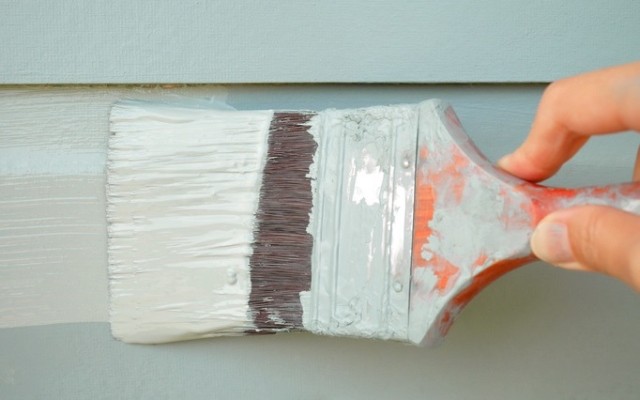 image of repainting a grey house with an off-white color coated paintbrush