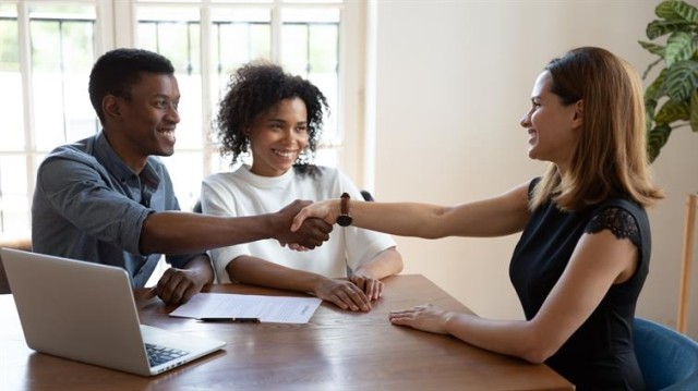 landlord shaking hands with a couple while seated at a table with a laptop