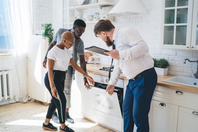 A couple and a man in a tie inspect an oven inside of a kitchen