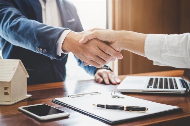 image of two people shaking hands over a document with a pen and keys on top of it