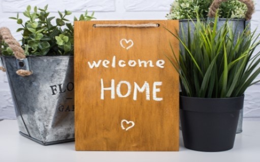 A sign displaying a "Welcome Home" message surrounded by house plants
