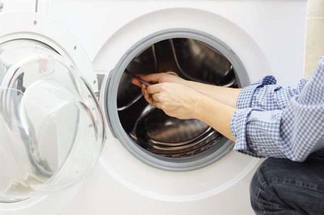 a person holding a tool and making a repair to a clothes washing machine