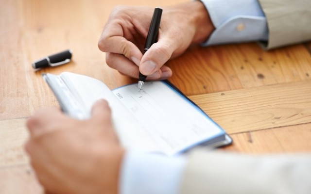 Someone wearing a business causal using a black pen to write a check within their checkbook