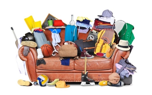A leather couch piled high with clothes and sports equipment