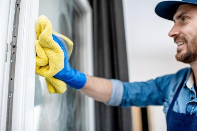 a professional cleaner cleaning a window surface with a chamois cloth while wearing protective gloves