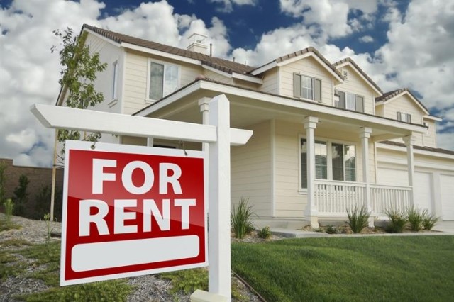 A two-story home in the suburbs with a For Rent sign displayed in the front yard