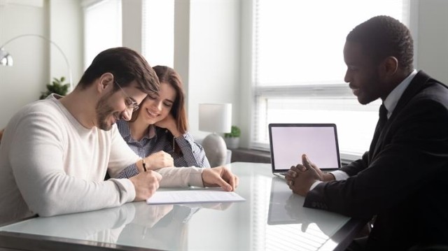 a couple signing a lease while sitting at a desk opposite of a landlord