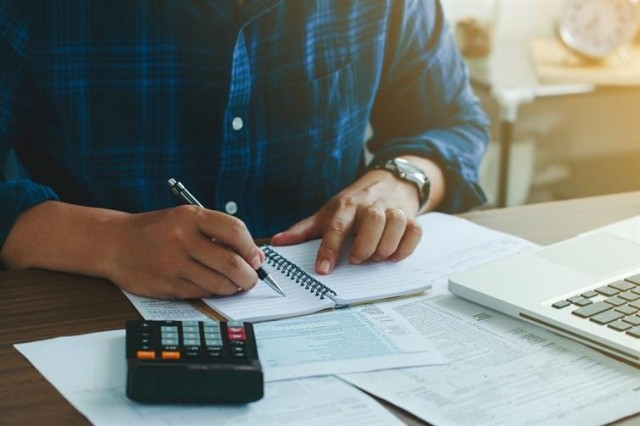 person at a desk with a calculator, laptop, and open notebook solving a math problem