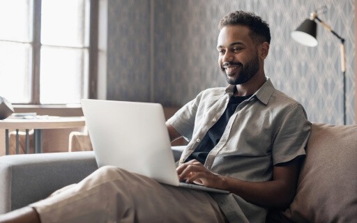 A young man browses on his laptop while sitting on a couch.