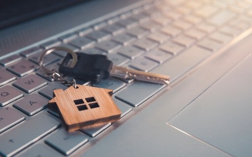 Key with a house keychain attached on top of a laptop keyboard.