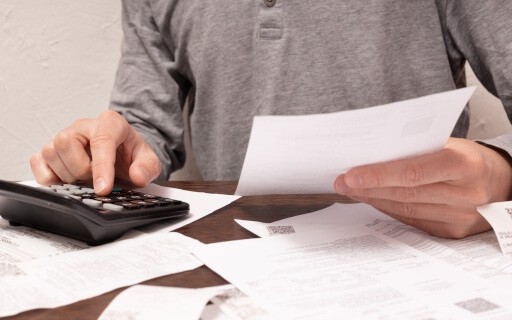 A person surrounded by papers does calculations.