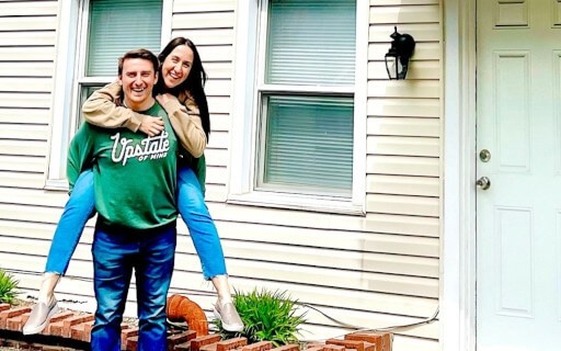 Ali and Josh Lupo (@theficouple on Instagram, Facebook, and TikTok) pose in front of property.