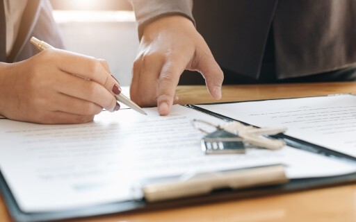 Close-up image of two people reviewing and signing a rental lease agreement with a key fob on the table, symbolizing apartment move-in.