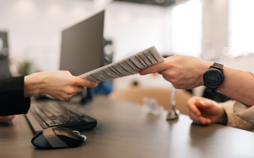 Tenant handing over a printed proof of renters insurance to leasing office staff member inside a modern apartment community office setting.