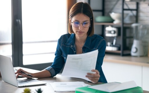 Woman reading over documents and using a laptop.