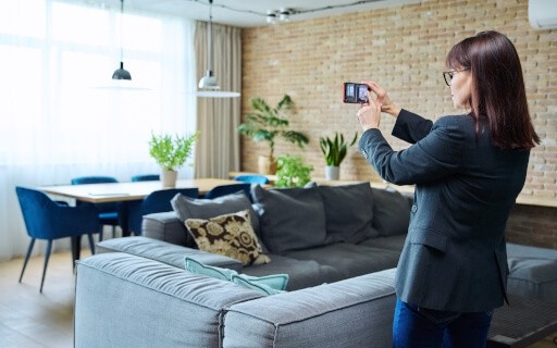 Woman in professional clothing photographing living room with smartphone..